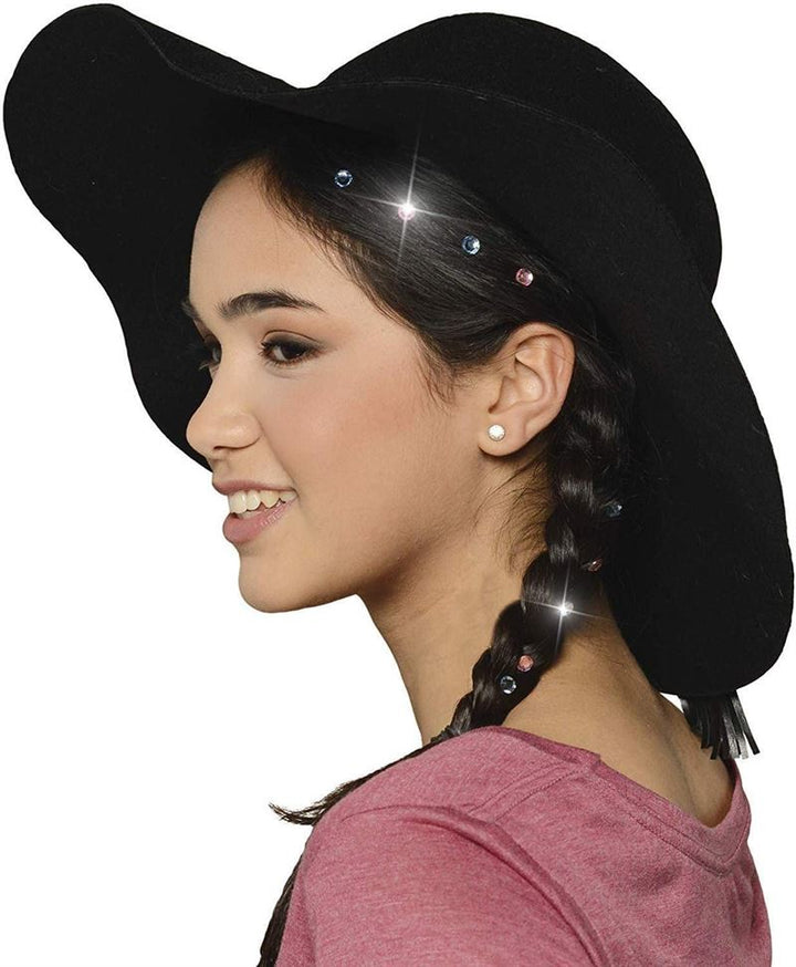 A young girl with braided hair decorated using Fashiongirls Bling Bling Ultimate Glam Kit—180 diamonds and styling tool—wears a wide-brimmed black hat and a pink top, smiling in profile against a white background.