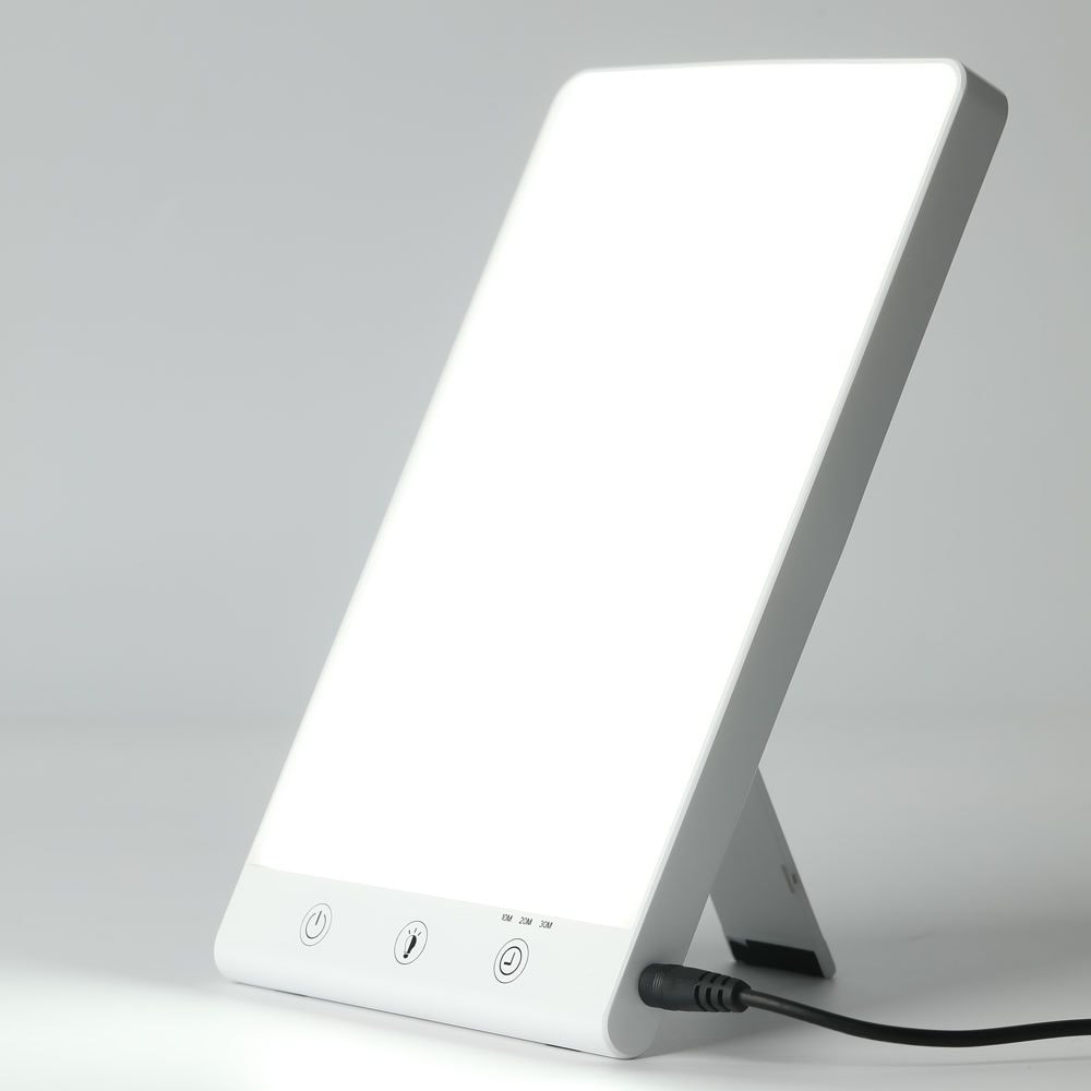 The Fashiongirl Light Therapy Lamp 10,000 lux LED is a rectangular lamp with a bright white screen, fold-out support, three control buttons, and a power cord at the bottom—designed to simulate artificial daylight.