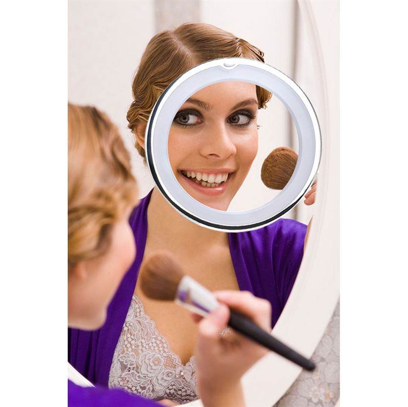A woman smiles as she applies makeup using the UNIQ PRO BEAUTY Bathroom Mirror with LED Light and Suction Cup x10 Magnifying Mirror in white, mounted on her larger bathroom mirror.