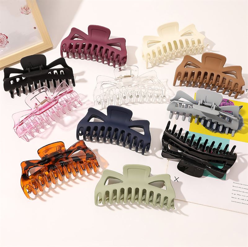 The SOHO Astrid Hair Claw - White by SOHO is a secure, large clip ideal for thick hair. Shown on a flat surface, the white claw overlaps paper and sits beside a photo frame for an elegant display.