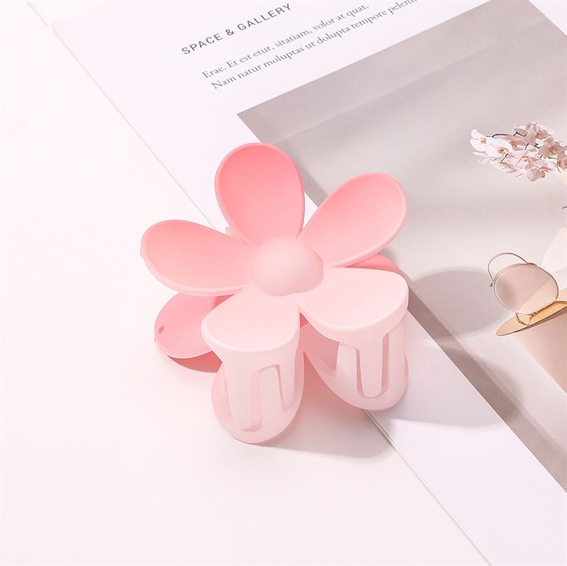 The SOHO Bloom Hair Claw - Pink Ombre by SOHO sits on an open magazine with a minimalistic interior design image—perfect for quick updos or adding a charming touch with this cute hair clip.