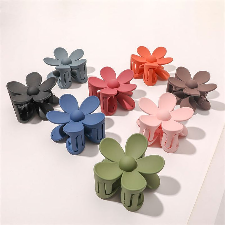 Eight SOHO Bloom Hair Claws by SOHO, including the yellow style and black, blue, green, pink, red, orange, brown, and light pink options, are arranged in a loose circle on a white surface.