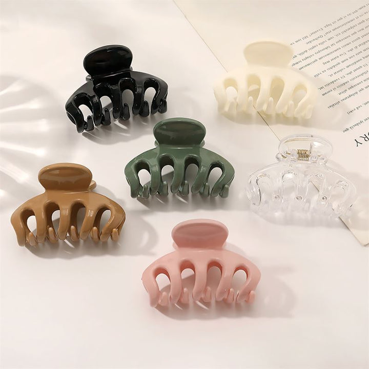 The SOHO Esta Hair Claw in green by SOHO is shown on a white surface beside an open book—ideal for reliable grip and stylish hairstyling.
