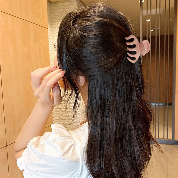 A woman with long dark hair, seen from behind, uses the SOHO Esta Hair Claw - Green to partially clip up her hair for extra grip. She wears a white top and stands indoors.
