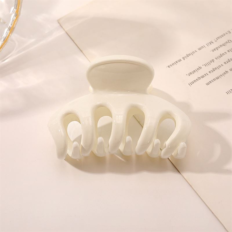 The SOHO Esta Hair Claw - White by SOHO, designed for extra grip, rests on a slightly angled piece of paper with printed text on a light-colored surface.