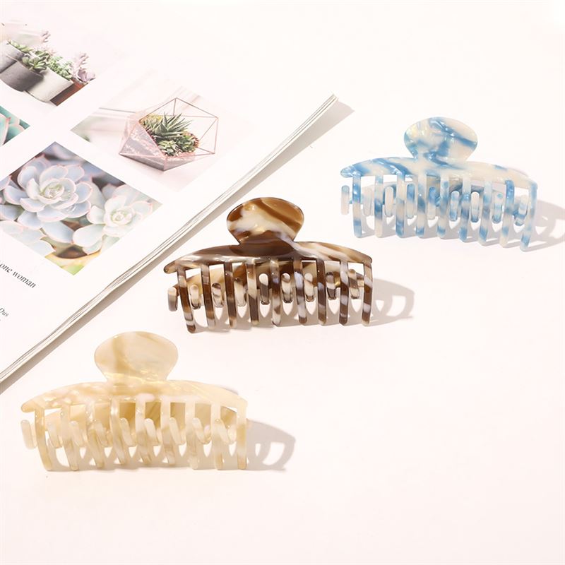 The SOHO Gaja Hair Claw in Beige Marble is displayed on a white surface beside an open magazine with succulent photos—ideal for elevating your style with this chic marbled hair accessory from SOHO.