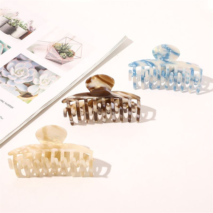 The SOHO Gaja Hair Claw in Beige Marble is displayed on a white surface beside an open magazine with succulent photos—ideal for elevating your style with this chic marbled hair accessory from SOHO.