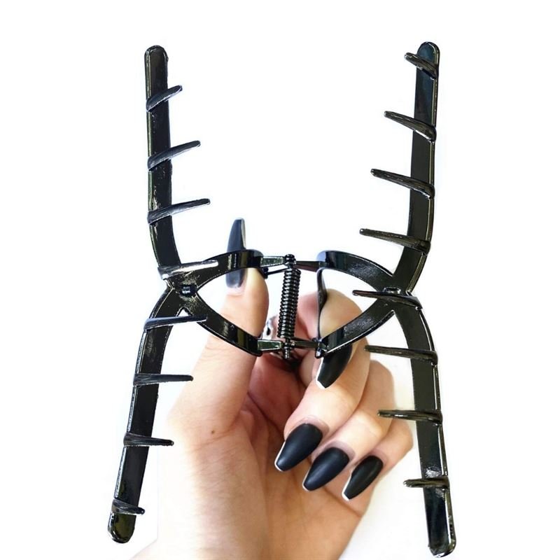 A hand with long, matte black nails holds the SOHO Iva Metal Hair Claw in Black, a large accessory by SOHO featuring widely spaced teeth—perfect for securing a messy bun—against a white background.