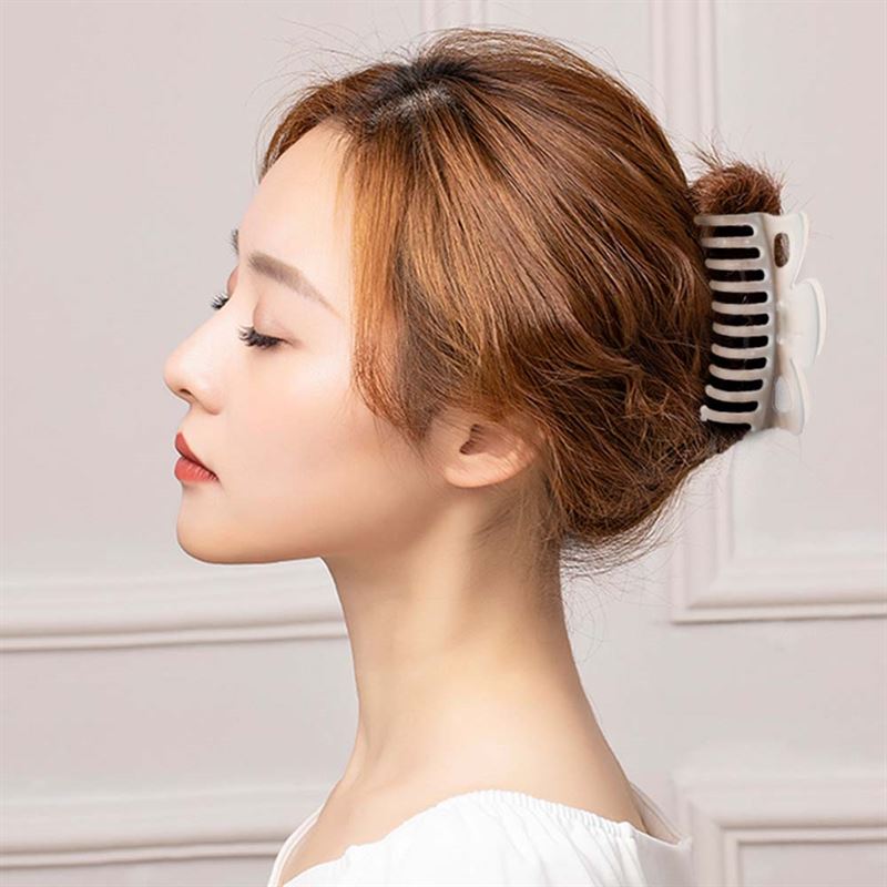 A woman with light brown hair in a bun, secured by the SOHO Jelly Hair Claw - Cool Blue from SOHO, is shown in profile against a neutral background. The stylish large claw offers a strong grip for all hair types. She wears a white top and looks serene.