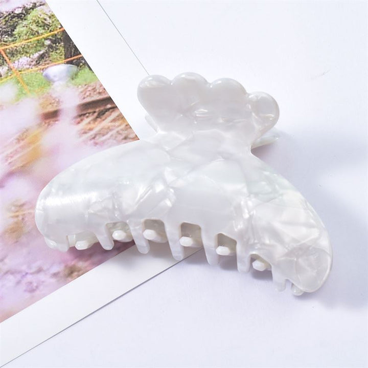 The SOHO Joy Hair Claw - Pure White by SOHO, an elegant acetate accessory, rests atop a partially visible photograph on a white surface.