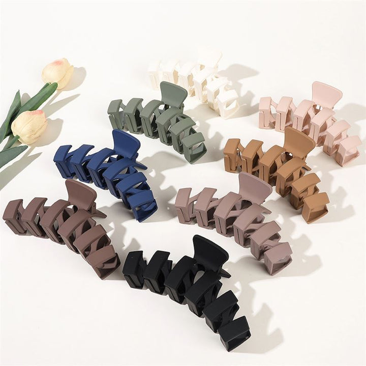 The SOHO Just Hair Claw - Black by SOHO is a large matte hair accessory, pictured on a white surface with two artificial tulips nearby, alongside other assorted colors like navy and mauve arranged in a semicircle.