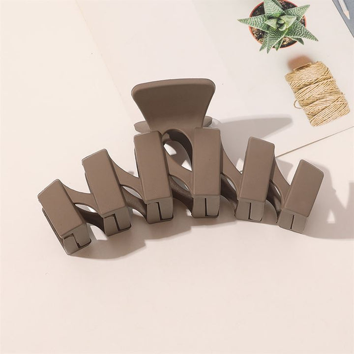 The SOHO Just Hair Claw - Brown by SOHO is displayed on a light surface next to a small potted succulent and a spool of twine.