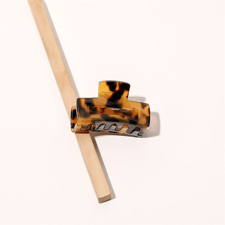 The SOHO Leia Mini Hair Claw - Tortoise by SOHO rests on a diagonally placed wooden stick against a light background, making it perfect for effortless hairstyling.