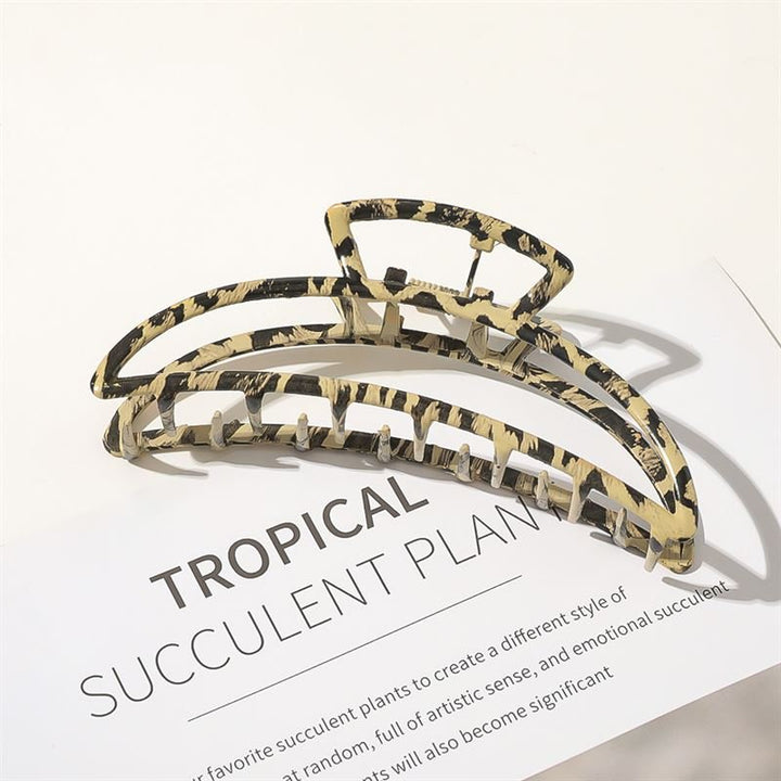 The SOHO Leopard Metal Barrette Hair Claw, featuring a beige and black tortoiseshell pattern, rests on a white surface partially covering a page with "TROPICAL SUCCULENT PLANT" in bold lettering.