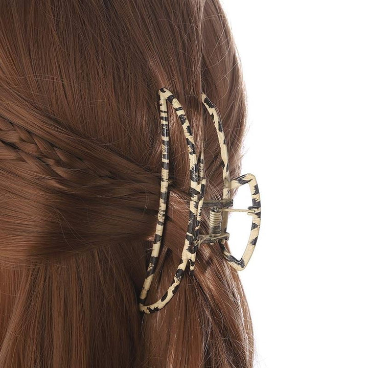 A close-up of brown hair styled with the SOHO Leopard Metal Barette Hair Claw, a large oval-shaped accessory by SOHO featuring a black and beige animal print. It securely holds hair in place, complemented by a small braid on one side.