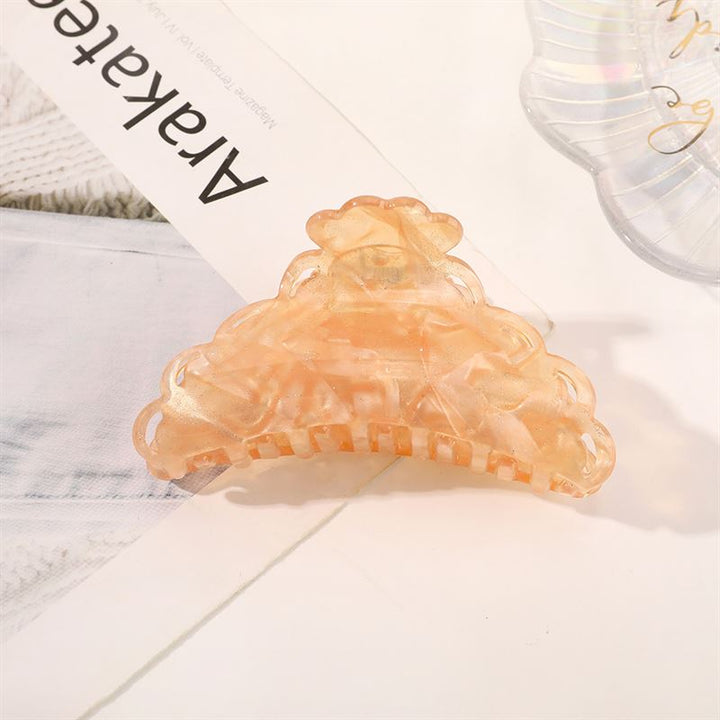 The SOHO Naomi Hair Claw - Sunshine by SOHO is a peach-toned, translucent hair accessory with a scalloped edge, shown on a white surface beside papers and another clear clip—ideal for adding elegance to any hairstyle.