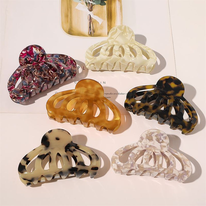 Six SOHO patterned hair claw clips, including the SOHO Olivia Hair Claw - Dark Tortoise, are arranged in a semicircle on a magazine, featuring marbled pink, cream, amber, tortoiseshell, black and white, and iridescent white designs.