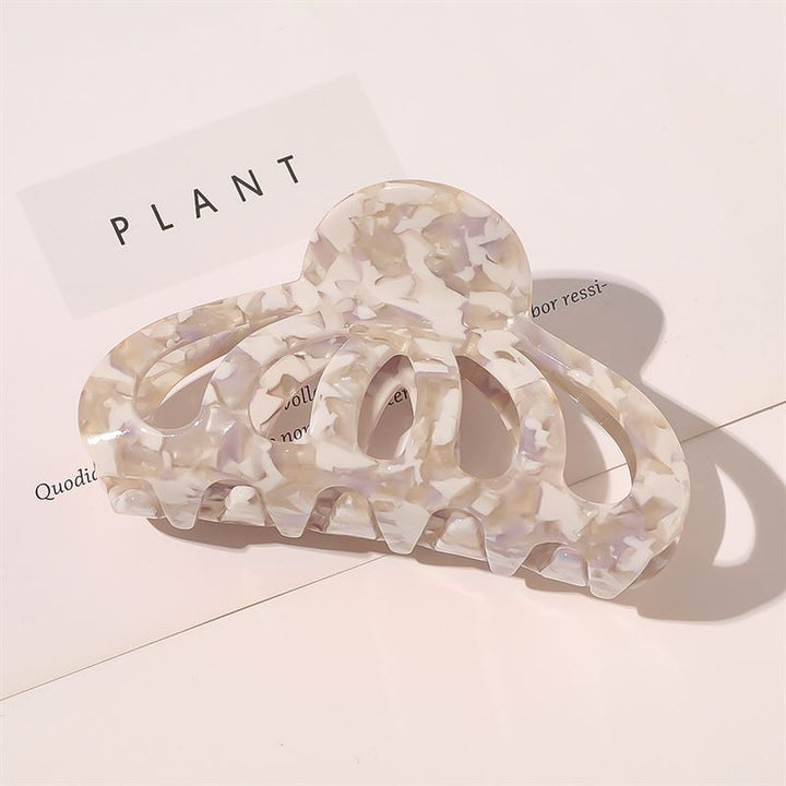 The SOHO Olivia Hair Claw - Marble, a pastel marble-patterned accessory by SOHO, sits on a white surface with printed text and gentle shadows, adding a chic touch to any style.