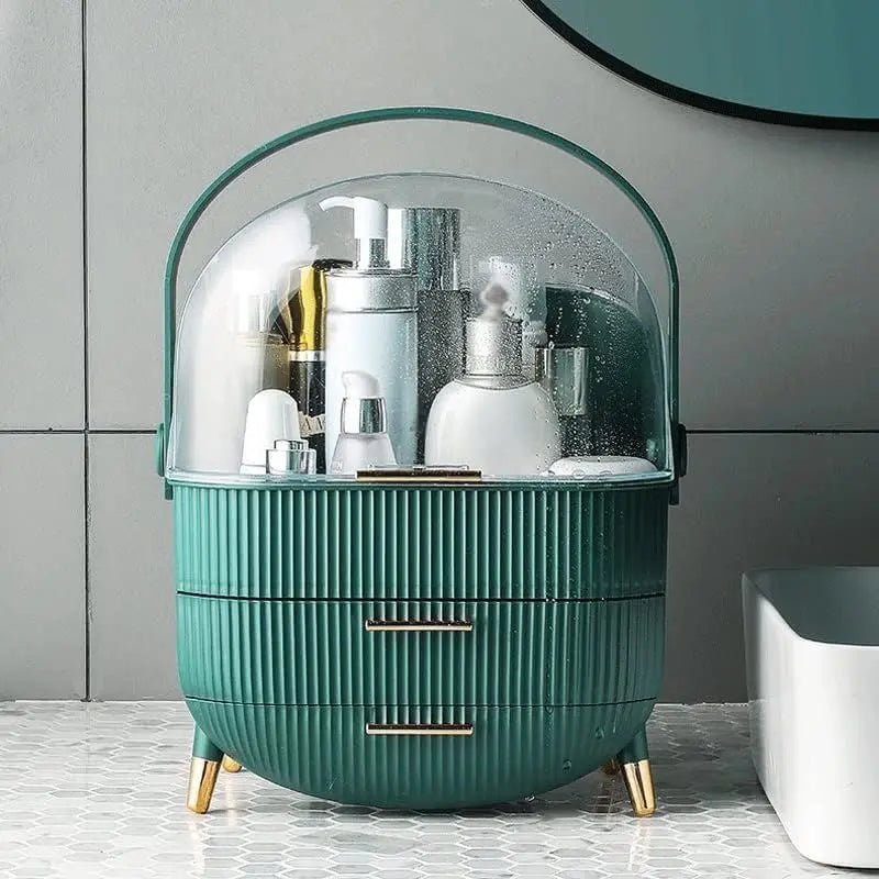 The UNIQ Retro Makeup Box Organiser in Dark Mint/Dark Green features ribbed sides, gold legs and handles, and a clear domed cover, perfect for storing skincare and cosmetics on your bathroom counter by the sink.